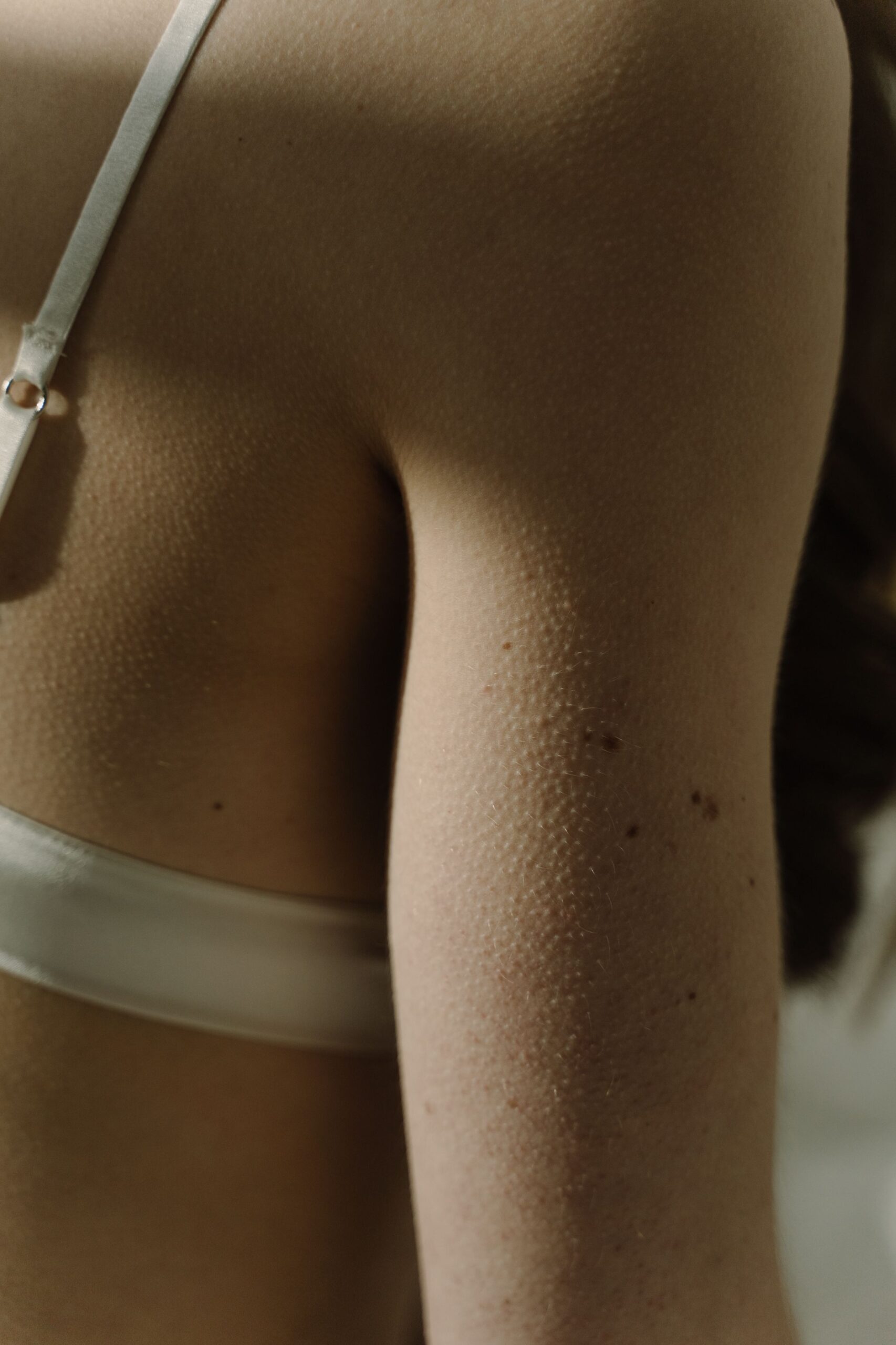 Intimate close-up capturing a woman's upper arm wearing a white bra, highlighting skin detail.